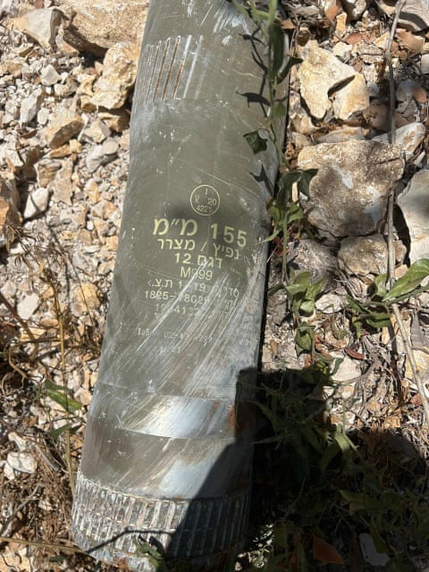 Hebrew lettering on a battered metal tube-like object which is lying on rocky ground.