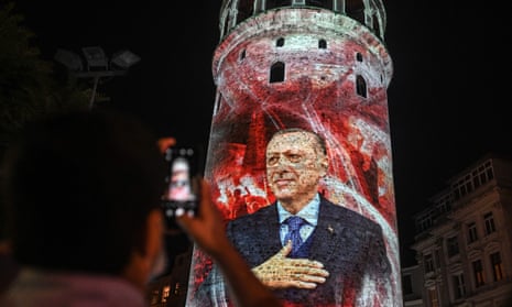 A man takes a picture of the Galata tower where is displayed a portrait of Turkish President Recep Tayyip Erdogan
