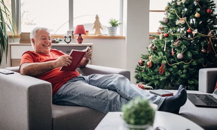 Older man reading a book by the Christmas tree at home
