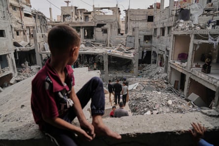 A boy looks out at a destroyed neighbourhood from the rubble of a house
