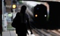 A woman in shadow waits on a platform as a train pulls in