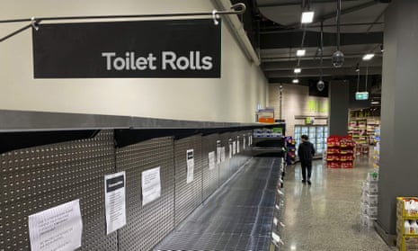 A shopper passes empty shelves usually stocked with toilet paper in a supermarket in Melbourne.