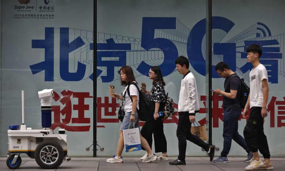 People walk toward a police robot mounted with surveillance cameras patrol past a 5G network advertisement