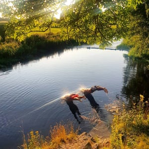Two swimmers dive into a river as sunlight hits the water