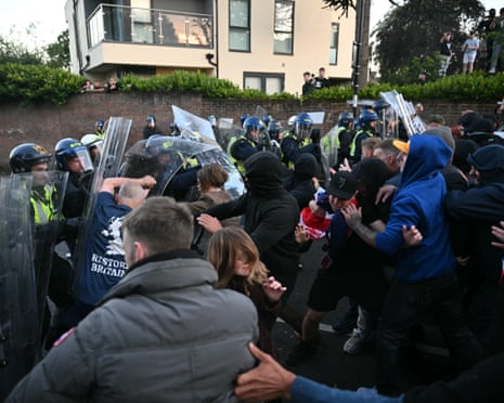 Riot police with shields face a crowd of protesters in a residential street