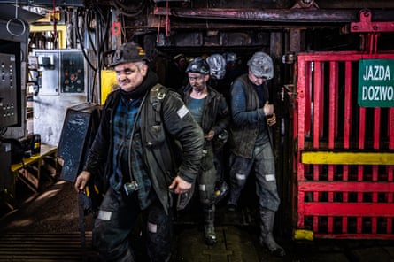 Miners wearing helmets and uniforms step out of a lift.