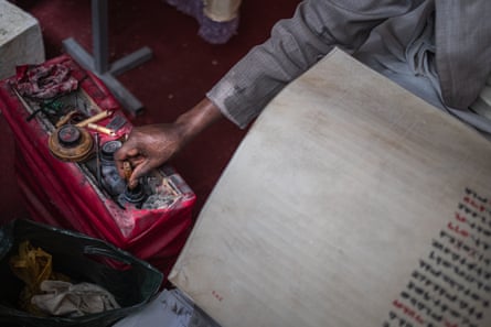 A man dips his bamboo pen into a well-used ink pot while working on a parchment written with ornate script