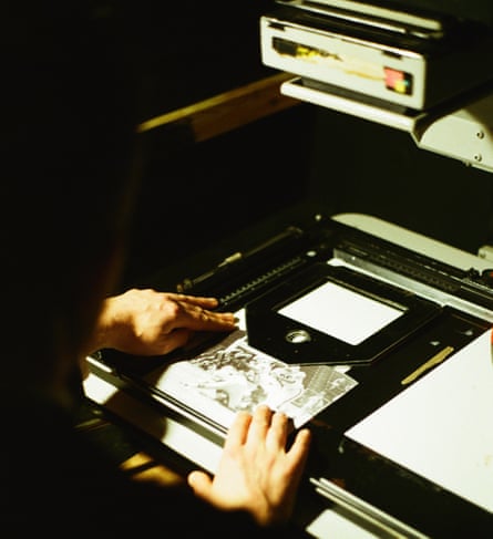 A shot of man showing just his hands and the back of his head as he examines a black and white photograph with some machinery.