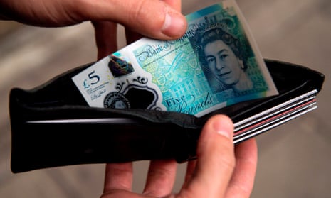 A person is pictured holding a wallet containing a £5 note