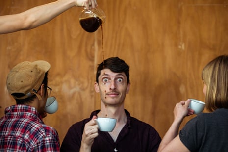 A man holding a cup of coffee, looking extremely wired, as someone pours coffee into the cup high from above