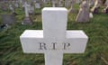 Close up of white stone grave in cross shape reading RIP in graveyard with other graves behind it