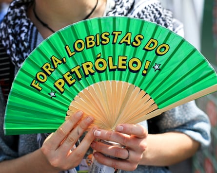 A person holds a fan with the phrase ‘Out with the oil lobbyists!’ in protest against oil companies at Cop30