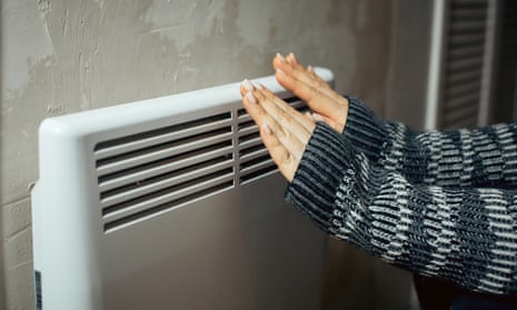 A woman warms her hands at the radiator in a cold house.