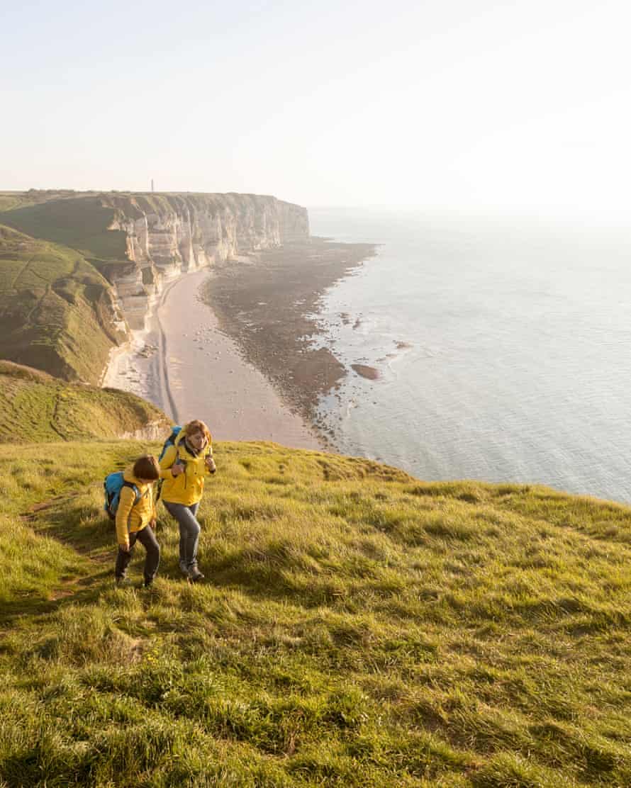 France, Normandy: Mother and son in yellow jackets hiking on cliffs covered with grass above the beach of Etretat
