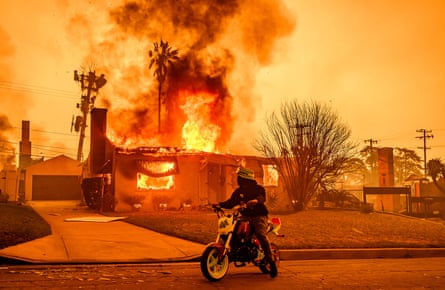 A motorcyclist stops to look at a burning home