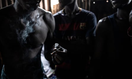 Topless men smoke joints of kush in a dark, dingy-looking spot.