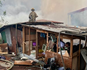 A firefighter on the roof of a damaged building with smoke billowing in the background