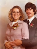 Woman in grey suit with brooch embraced by man in dark suit