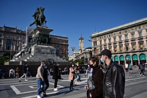 People wearing protective masks walk across the Piazza del Duomo in Milan.