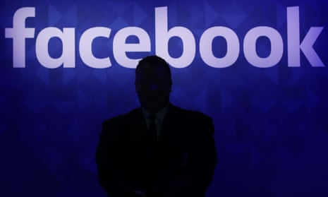 A silhouette of a person in front of a Facebook sign