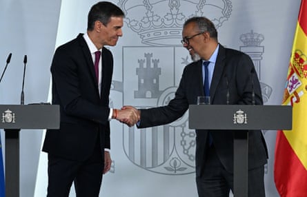 Sánchez and Tedros, standing behind lecterns, shake hands. The spanish flag is on the right of the picture
