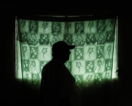 A. man in a cap seen in silhouette against a green and white curtain against a window.