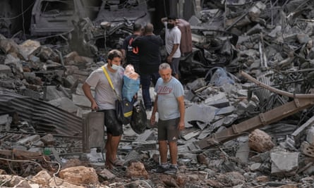 Residents walking on the rubble of destroyed buildings with their belongings at the site of Thursday’s Israeli airstrike, in Beirut.
