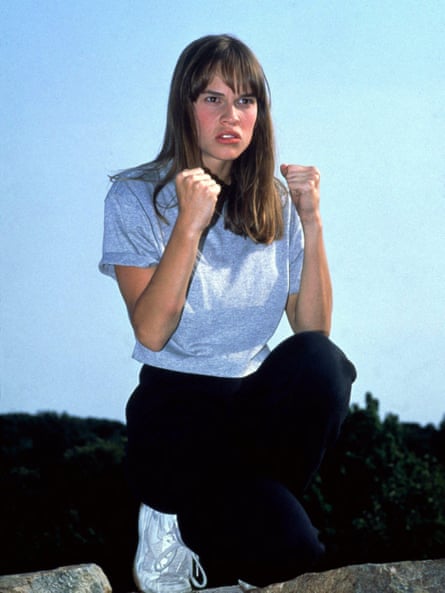 Hilary Swank crouched with fists up wearing a grey T-shirt, dark jogging trousers and white trainers