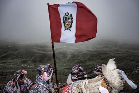 A group in traditional dress gathers during the Compadres festival, holding a Peruvian flag aloft.