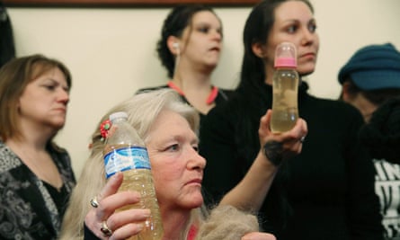 Flint residents, including Jessica Owens, right, holding a baby bottle full of contaminated water, are seen during a news conference in Washington DC. Williamson, and Owens traveled to Washington by bus with other Flint families to attend the House hearing on the crisis.