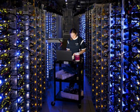Google technician checks a laptop between illuminated server racks in a datacentre