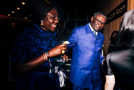 A man and a woman in evening clothes and holding drinks smile as they talk at a party.