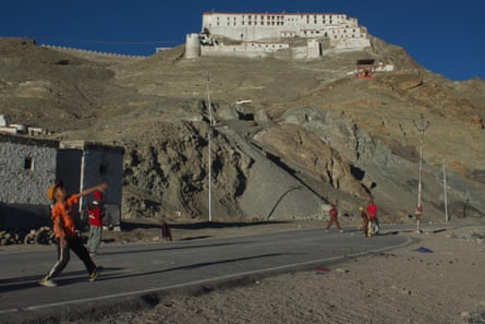 Children play cricket on a road with a white imposing building on a hill behind them