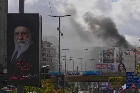 A portrait of Iran's late supreme leader Ali Khamenei, left, as smoke rises following an Israeli airstrike in Dahiyeh, on 30 March 2026.