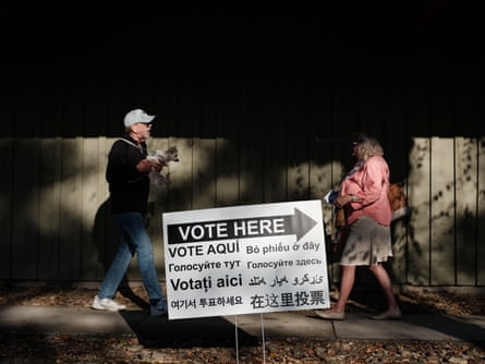 pair walk toward each other behind ‘vote here’ sign. man’s carrying small dog
