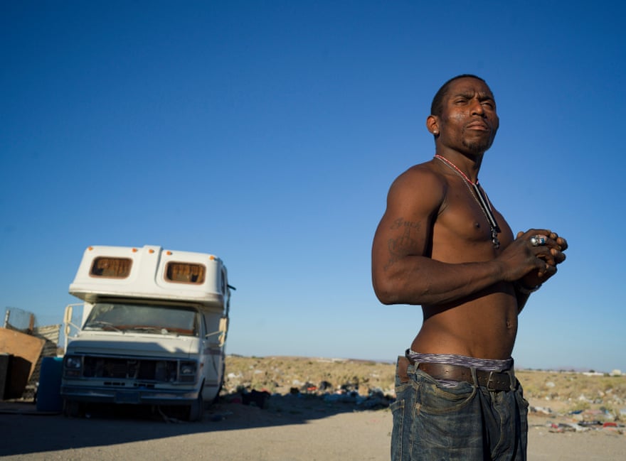 A shirtless man stands for a portrait, an RV in the background