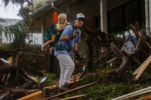 A search and rescue worker with a child on her back looks through debris