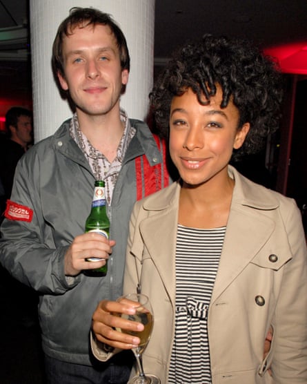 A white man and black woman smile at the camera while holding their drinks.