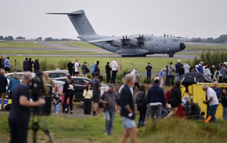 People gather behind the fence at the airport, as a large RAF transport plane sits on the tarmac