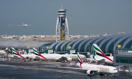 An Emirates jetliner comes in to land at Dubai International airport; the control tower, a terminal building and parked planes are seen in the foreground and the city is seen in the far distance