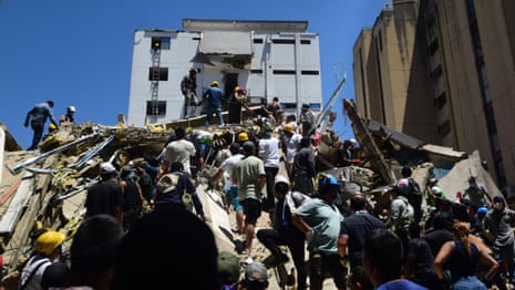 A crowd of people milling over large pile of rubble