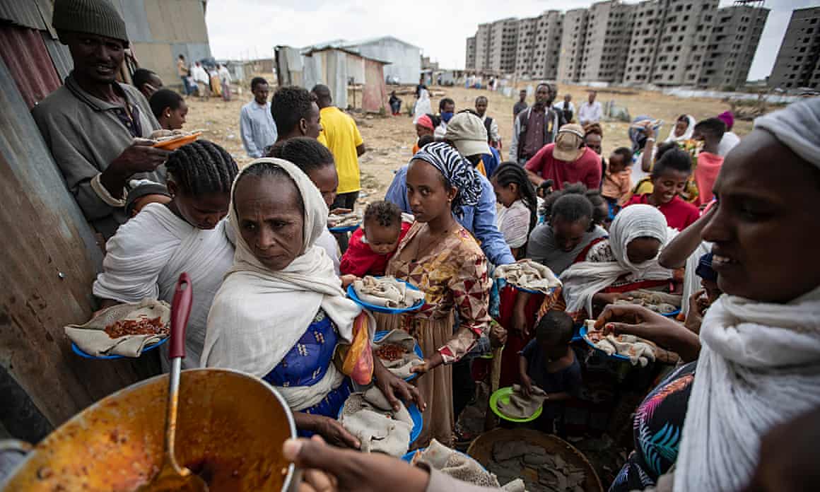 People holding plates and bowls queue for food handouts