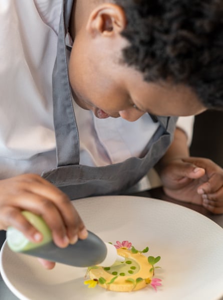 A young African woman leans over a plate adding sauce