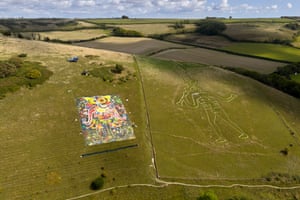 An aerial shot of a large, brightly coloured artwork laid out on a hillside next to ancient chalk carving