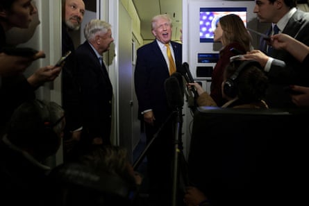 Trump in the corridor of Air Force One talking to journalists with microphones held out.