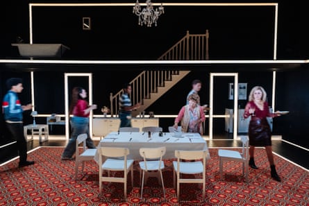 Stage set from Ilford Boy showing a dining room with chandelier, staircase, and people moving around a set table