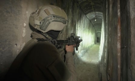 Israeli soldier points assault rifle ahead of him down a narrow illuminated tunnel