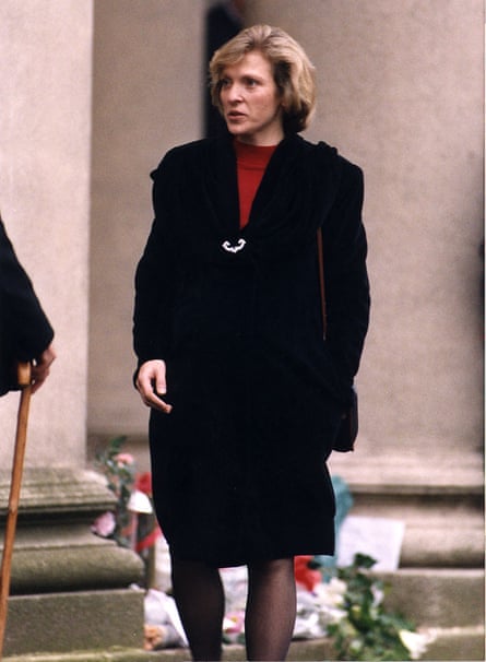A blond woman in a dark coat and red jumper