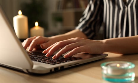 A woman's hands typing on a laptop with candles burning beside her