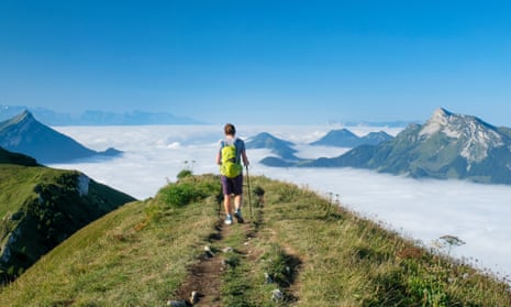 Hiker on a ridge of Mont Trélod on a blue-sky day. He is above the clouds and surrounded by mountain peaks in the French Alps.